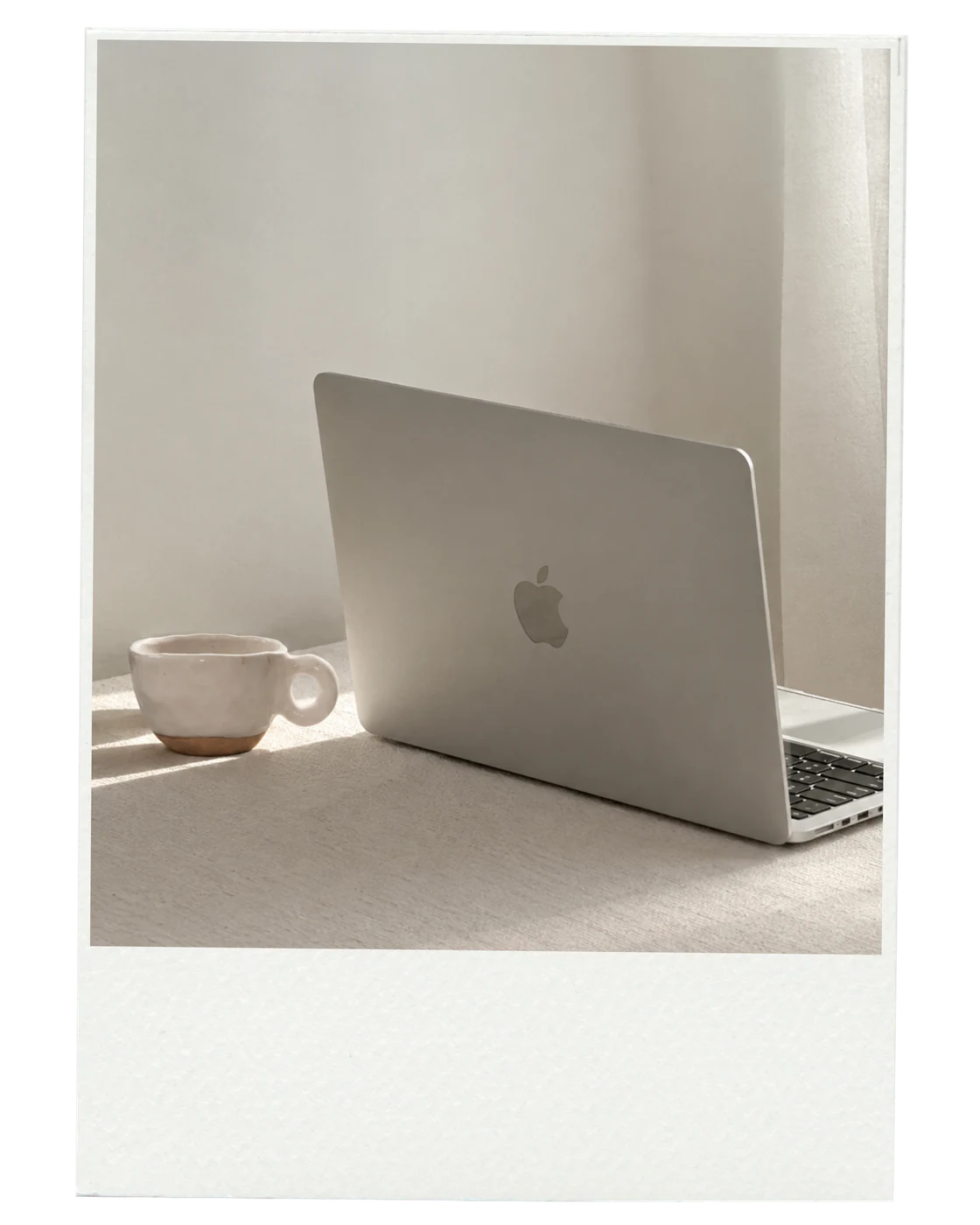 A silver laptop and ceramic cup on a sunlit table, shown in a polaroid frame